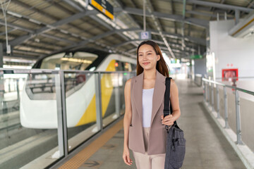 Portrait of a young asian woman with laptop bag in front a public skytrain in a subway terminal