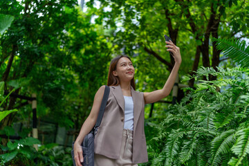 Asian Woman With Laptop Bag Using Phone Amid Greenery in A Park In the City