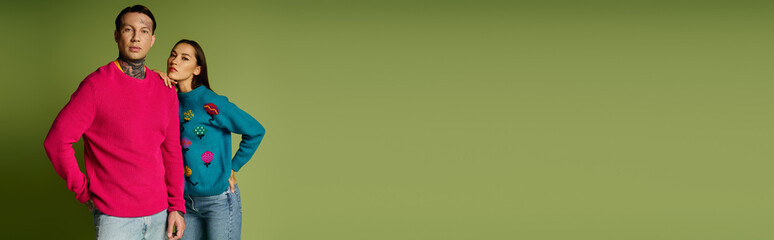 Fototapeta premium A stylish young couple showcases trendy sweaters while posing in front of a green backdrop.