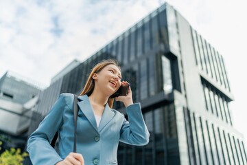 Asian Businesswoman Carrying Laptop Bag Using Phone In Front Of A Modern Office Building