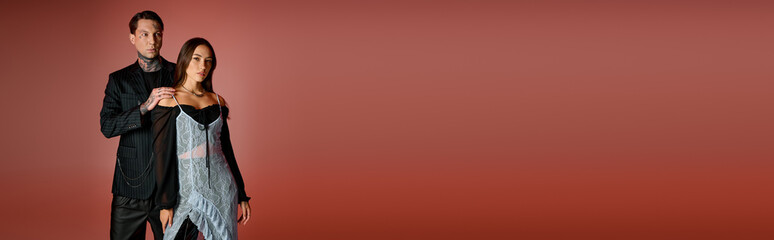 A stylish young couple stands close, showcasing modern fashion on a warm background.