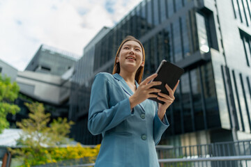Fototapeta premium Young Businesswoman Using Digital Tablet In Front A Modern Office Building in a Financial District