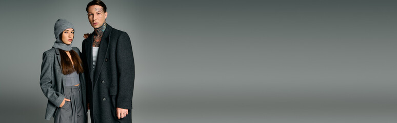 A young couple, dressed in fashionable winter clothing, stands confidently together.