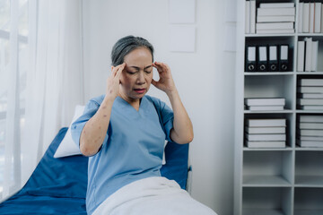 Patient in Distress: Elderly woman in light blue scrubs experiencing intense head pain, sitting on...