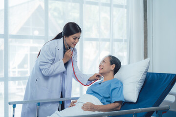 Compassionate Care: A female doctor attentively listens to her elderly patient's heartbeat with a...