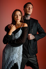 Couple exudes confidence and style in a trendy urban setting against a striking red backdrop.