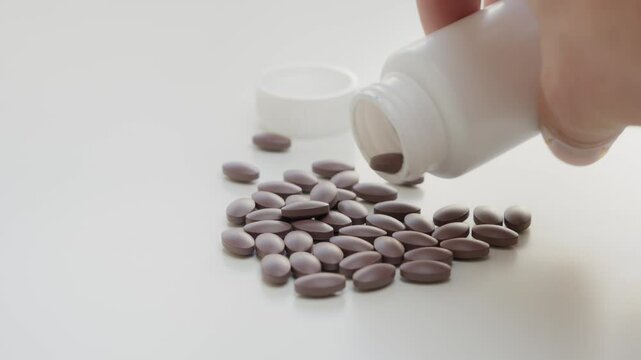 A white bottle is seen spilling brown tablets onto a white surface, depicting a concept of medication, healthcare, or supplements. The image highlights medicine and pharmaceutical themes.