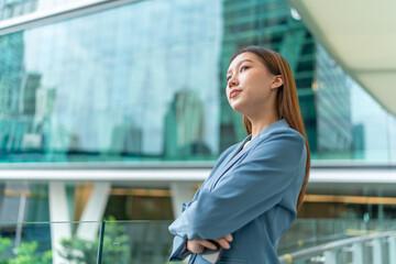 Young Businesswoman Holding Phone and Standing In Front A Modern Office Building, Looking Contented