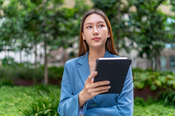 Fototapeta premium Young Asian Businesswoman Using Digital Tablet Outdoor In Front Modern Office Building