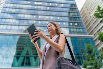 Young Asian Woman Using Tablet In Front A Modern Glass Office Building in Downtown Financial District