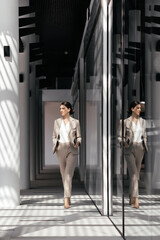 Side view of Caucasian middle-aged business woman wearing beige suit walking along office hall outdoor. Successful woman entrepreneur. Productive business meeting in a corporate workplace.