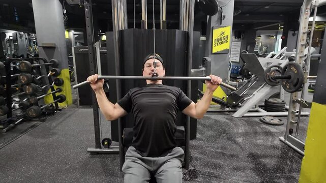 Moving Top View of Handsome Man Performing Front Lat Pulldown on Gym Machine, Targeting Back Muscles and Focusing on Back Development During Workout