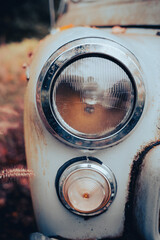 Zbliżenie na przednie światła antycznego samochodu w jesiennej scenerii – retro motoryzacja w otoczeniu złotych liści, tworząc unikalny klimat pełen ciepłych barw i nostalgii.