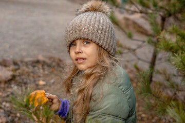 A little girl wearing warm clothes in a forest park collects colorful autumn leaves. Autumn vibe, outdoor activities in autumn.