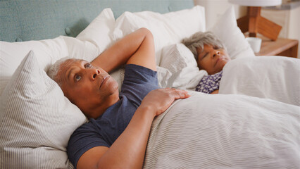 Worried Senior Man In Bed At Home Waking Up Next To Wife In Morning