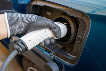 Electric car charger plugged in a blue car and a hand on globes holding it. Close up picture