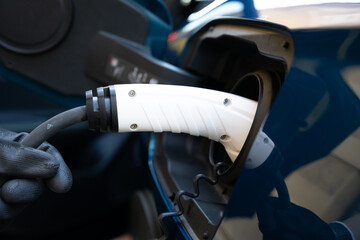 Electric car charger plugged in a blue car and a hand on globes holding it. Close up picture
