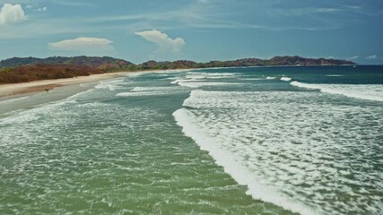 Flying low over the long stretching beach in Nosara, Costa Rica. View of the big waves coming to the shore. Destination of surfers and water sports enthusiasts.