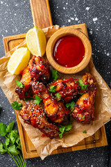 Spicy chicken wings with sriracha sauce and lime on a cutting board on dark background top view