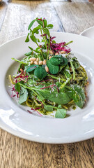Green pesto pasta spaghetti garnished with basil leaf served on a white plate