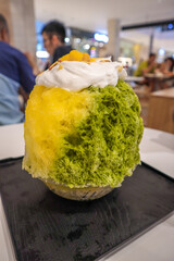 A bowl of kakigori Japanese shaved ice dessert of mango and green tea matcha flavour topped with whipped cream and mango bits