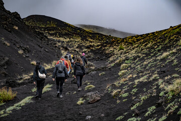 Photography of A group of hikers in outdoor gear hiking and climbing the dark and rocky, barren slopes of Mount Etna, Sicily. during a foggy and cloudy day. Stock photo