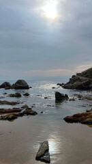 Plage de sable sur la côte espagnole de la Méditerranée au soleil couchant sous un ciel nuageux et orageux d'automne avec des rochers affleurant et un chemin côtier de promenade touristique.