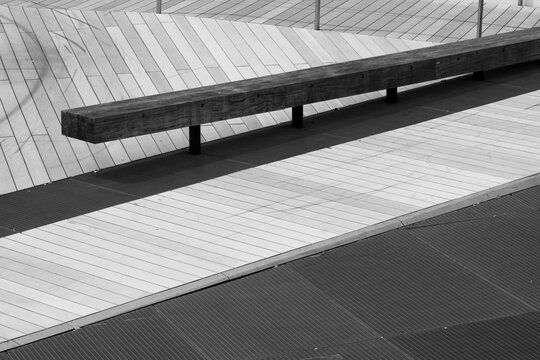 A striking outdoor scene featuring a long wooden bench on a meticulously patterned surface, combining straight lines and geometric designs, offering a contemporary atmosphere.