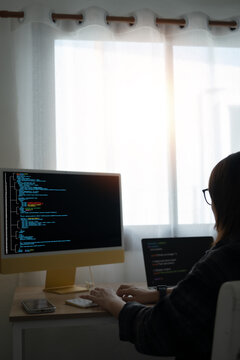 Coding Computer Programmer, A woman sits at a table with a computer monitor and laptop in front of her. She was typing on the keyboard and looking at the computer screen.