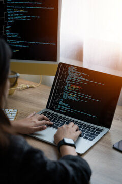 Coding Computer Programmer, A woman sits at a table with a computer monitor and laptop in front of her. She was typing on the keyboard and looking at the computer screen.