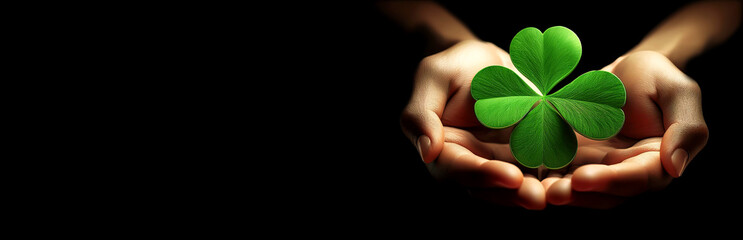 Extreme close-up of female cupped hands holding a beautiful large green four leaf clover, lucky symbol, isolated on a black background with copy space, blank wide banner. Generative Ai.