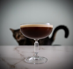 Expresso Martini cocktail with a blurt cat behind and reflected in small shapes on the glass. above marble white table 