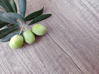 Natural fresh green olives on a branch with leaves on a wooden background