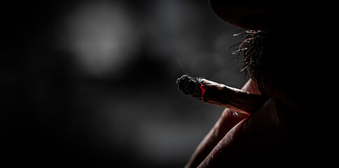 close-up man with cigar in his mouth and holding with two fingers. 