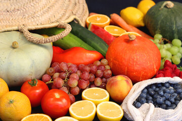 Round straw bag and various seasonal fruits and vegetables on dark background. Summer and fall produce. Selective focus.