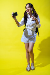 An Asian woman in a white shirt and striped shorts, holding a camera while enthusiastically...