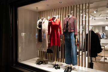 Female mannequins in store glass window display dressed casual autumn — winter elegant clothing, night scene.