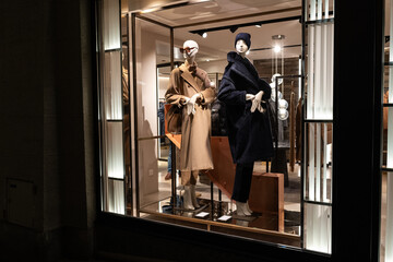 Female mannequins in store glass window display dressed casual autumn — winter elegant clothing, night scene.