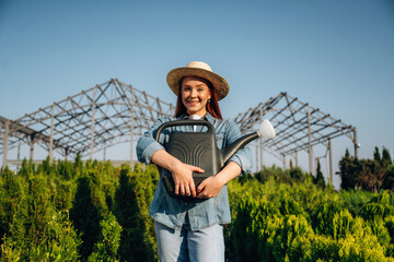 Watering can. Young redhead woman is taking care of garden