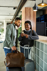 A young couple excitedly discusses their vacation plans while in a trendy hotel lobby, filled with anticipation.