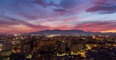 Vibrant city skyline at twilight with glowing lights, silhouetted mountains, and a colorful pink, purple, and blue sky.  urban, travel, and scenic concepts.