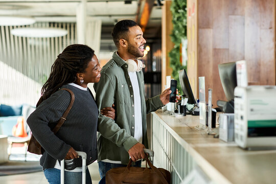 A young African American couple joyfully checks in at a hotel lobby, excited for their vacation getaway.