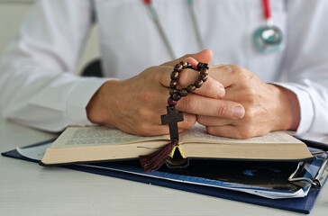 A medical worker holds a rosary with a cross and meditates