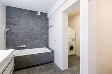 modern, minimalist bathroom features white tiles and grey stone tile accents.  A white vanity, bathtub, toilet and bidet create a clean, spacious feel.  The lighting is bright and contemporary