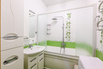 interior apartment bright, compact bathroom features a white bathtub/shower combo with frosted glass doors, green tile accents, and a modern white washing machine.  