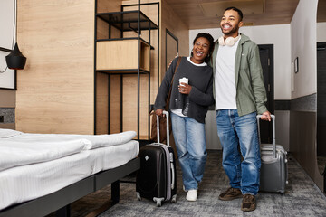 A young couple embraces happiness while unpacking their bags in a stylish hotel room during their vacation.