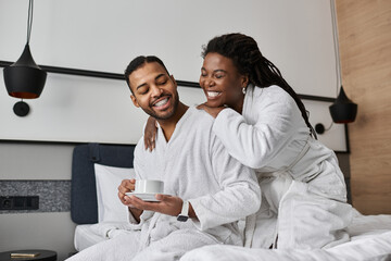 A loving couple shares a warm moment, sipping coffee and smiling in their hotel suite while on vacation.