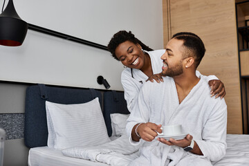 A young African American couple shares a joyful moment together in their hotel room, radiating love and happiness.