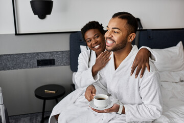 A loving couple embraces in bathrobes, sharing a warm moment with coffee during their hotel getaway.