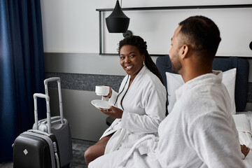 A cheerful young couple shares a romantic morning, sipping coffee while relaxing in their hotel...